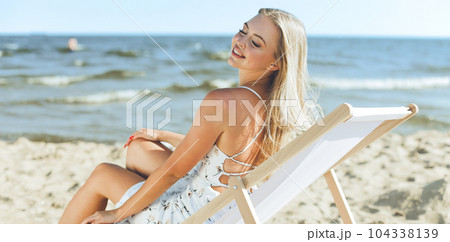 Happy blonde woman relaxing on a wooden deck chair at the ocean beach 104338139