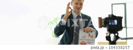 Business coach man showing ok gesture and holding papers with charts in front of camera Business coach man showing ok gesture and holding papers with charts in front of camera 104338257