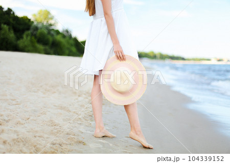 Young woman on a beach holding a white hat. Legs close up 104339152
