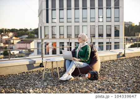 Woman working on gadget connected to battery on terrace 104339647