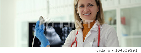 Smiling woman doctor holding ultrasound probe in hands to diagnose early pregnancy in clinic 104339991