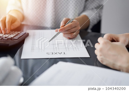 Woman accountant using a calculator and laptop computer while counting taxes for a client. Business audit and finance concepts 104340200