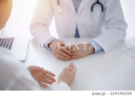 Doctor and patient discussing current health questions while sitting opposite of each other at the table in clinic, just hands closeup. Medicine concept 104340209