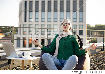 Adult in hijab meditating in bean bag in rooftop workplace 104340314