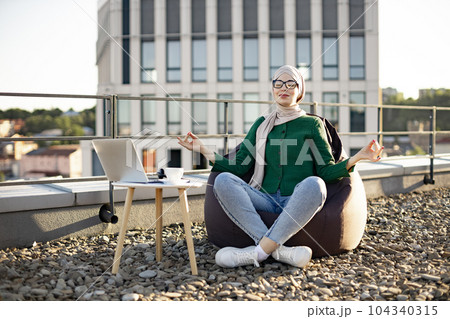 Adult in hijab meditating in bean bag in rooftop workplace 104340315