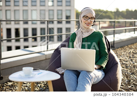 Arabian lady in headset staying with computer on terrace 104340384