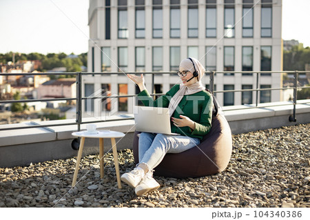 Woman in hijab running web conference via devices on rooftop 104340386
