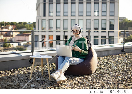 Woman in hijab running web conference via devices on rooftop 104340393