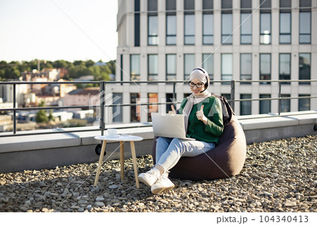 Woman in hijab running web conference via devices on rooftop Woman in hijab running web conference via devices on rooftop 104340413