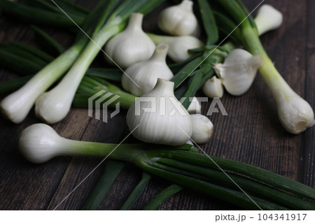 Fresh garlic and onions on the table. Kitchen still life with heads of garlic. Vegetables ingredients for a recipe on a kitchen board Fresh garlic and onions on the table. Kitchen still life with heads of garlic. Vegetables ingredients for a recipe on a kitchen board 104341917