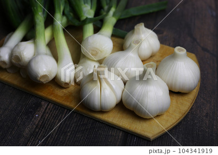 Fresh garlic and onions on the table. Kitchen still life with heads of garlic. Vegetables ingredients for a recipe on a kitchen board 104341919