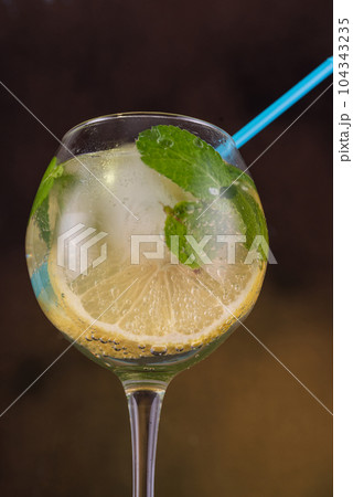 Macro photo of a wine glass with lemon and mint. A straw in a wine glass. 104343235