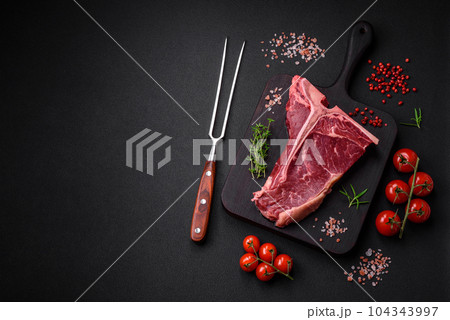 Raw juicy beef t-bone steak with salt, spices and herbs 104343997