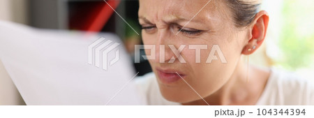 Focused woman trying read papers, squinting to see more clearly Focused woman trying read papers, squinting to see more clearly 104344394