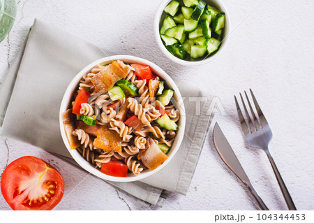 Hearty salad of pasta, cherry tomatoes, cucumbers and fried bacon in a bowl top view 104344453