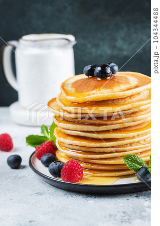 Delicious pancakes, with fresh blueberries, raspberry and maple syrup or honey on a dark background 104344488