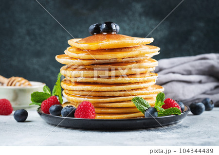 Delicious pancakes, with fresh blueberries, raspberry and maple syrup or honey on a dark background 104344489