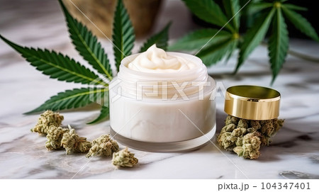 Jar of face cream stands on a marble background, surrounded by marijuana leaves 104347401
