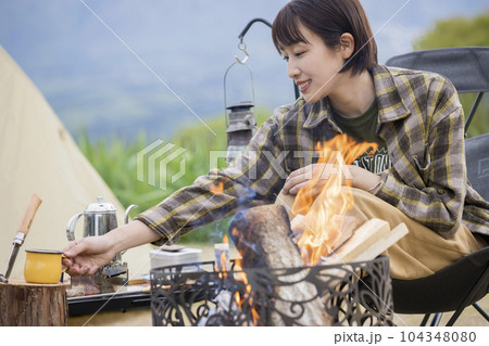 焚火の前でのんびりする若い女性　アウトドア　ソロキャンプ　チェアリング 104348080
