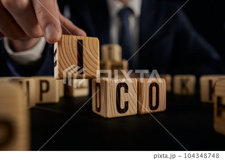 ICO symbol. Businessman hand turns wooden cubes ICO. on a black background ICO symbol. Businessman hand turns wooden cubes ICO. on a black background 104348748
