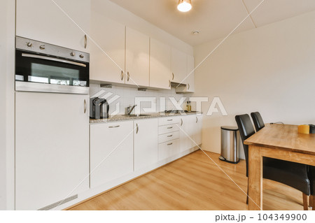 a kitchen and dining area in a house with white cabinets, wood flooring and an oven on the wall 104349900
