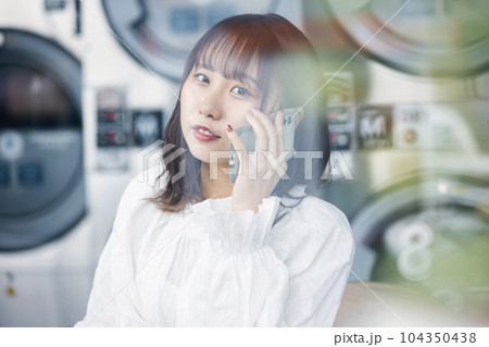 コインランドリーで電話をかける若い女性 コインランドリーで電話をかける若い女性 104350438