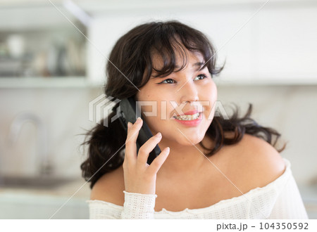 Portrait of smiling female who is talking by phone in kitchen at home 104350592