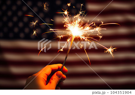 Patriotic Sparkler Spectacle: Hand Holding Lit Sparkler in Front of the American Flag for 4th of July Celebration. created with Generative AI 104351904