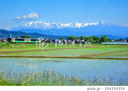 飯豊連峰を背景に会津盆地を走る只見線の列車キハE120形(福島県会津坂下町、5月下旬午前) 104354359