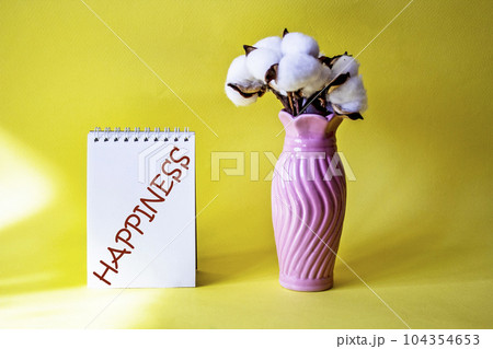 Happiness, the word is written on a notebook and a yellow background, next to a vase of flowers. Happiness, the word is written on a notebook and a yellow background, next to a vase of flowers. 104354653