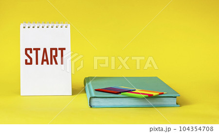 The word START is written on a notebook that stands on a yellow background, next to a notebook  104354708