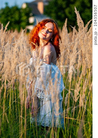 red-haired beautiful girl sits with her back in black, long dress in the grass 104356507