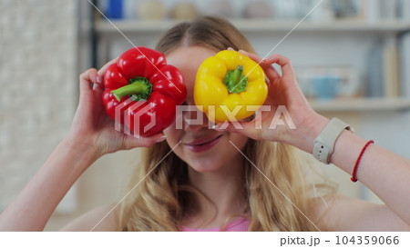 Close up of beautiful woman with fresh red and yellow peppers in her hands laughs and looks into the camera. Healthy lifestyle and dieting concept. Close up of beautiful woman with fresh red and yellow peppers in her hands laughs and looks into the camera. Healthy lifestyle and dieting concept. 104359066