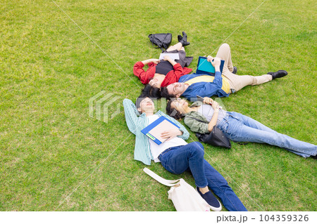 芝生に寝転んで空を見上げる多国籍の人々 104359326