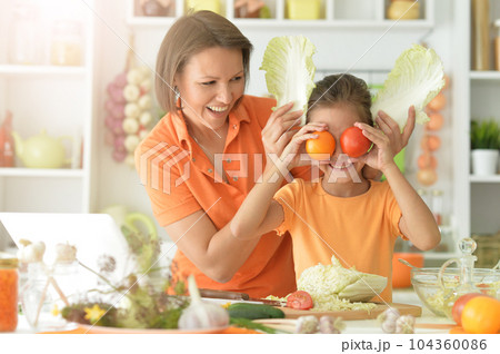 Portrait of girl with her mother cooking together at kitchen table 104360086