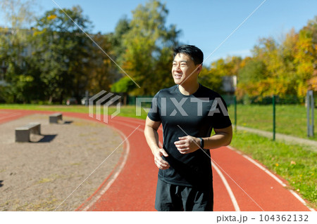 Young successful asian man jogging at daytime in stadium, man running and doing fitness active exercise in sports suit, active lifestyle. 104362132