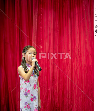 The Asian kid girl sing a song on stage at her school activity day, dress in Qipao style, red curtain background 104362269