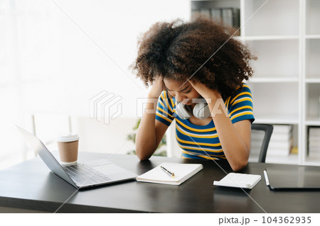 African woman feeling migraine head strain.Overworked businesswoman financier while working on laptop and tablet at office. African woman feeling migraine head strain.Overworked businesswoman financier while working on laptop and tablet at office. 104362935