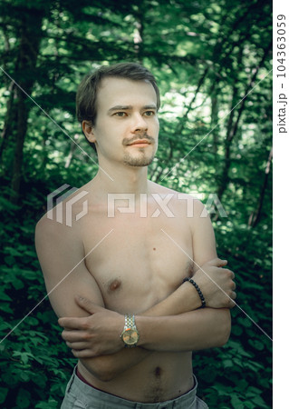 Waist up portrait of cheerful young man with beard standing topless in park. He is holding hands crossed on chest while wearing hand watch. Sport for body beauty concept. High quality photo Waist up portrait of cheerful young man with beard standing topless in park. He is holding hands crossed on chest while wearing hand watch. Sport for body beauty concept. High quality photo 104363059