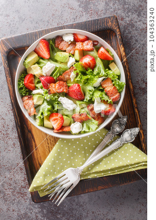 Summer salad of strawberries, avocado, bacon, lettuce, goat cheese close-up in a bowl. Vertical top view Summer salad of strawberries, avocado, bacon, lettuce, goat cheese close-up in a bowl. Vertical top view 104363240