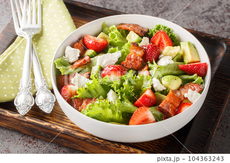 Salad with fresh strawberries, avocado, feta, bacon and lettuce on a wooden board close-up. Horizontal 104363243