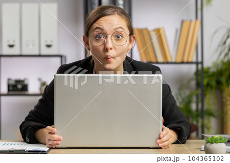 Office businesswoman hiding behind laptop computer making funny silly face fooling around disrespect Office businesswoman hiding behind laptop computer making funny silly face fooling around disrespect 104365102