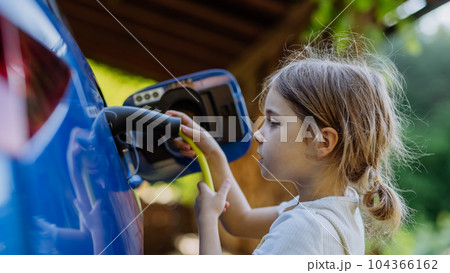Little girl holding power supply cable and charging their electric car. Little girl holding power supply cable and charging their electric car. 104366162