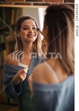 Young woman doing her make-up, looking in mirror. Young woman doing her make-up, looking in mirror. 104366429