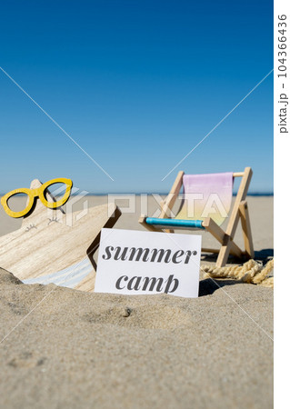 SUMMER CAMP text on paper greeting card on background of beach chair lounge starfish summer vacation decor. Sandy beach sun coast. Holiday concept postcard. Travel SUMMER CAMP text on paper greeting card on background of beach chair lounge starfish summer vacation decor. Sandy beach sun coast. Holiday concept postcard. Travel 104366436
