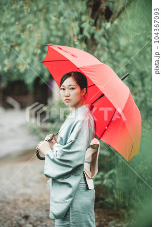 自然溢れる中で赤い傘をさす和服の若い女性 104367093