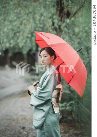 自然溢れる中で赤い傘をさす和服の若い女性 104367094