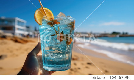 Blue refreshing cocktail at the beach in the woman hand on tropical beach background. 104367990