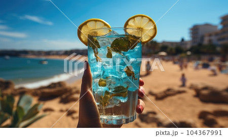 Blue refreshing cocktail at the beach in the woman hand on tropical beach background. 104367991