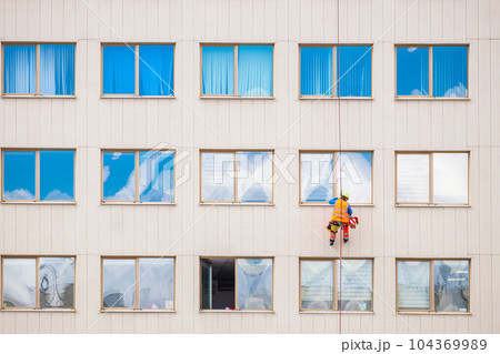 Industrial climber washes windows on facade of a building. Front view 104369989